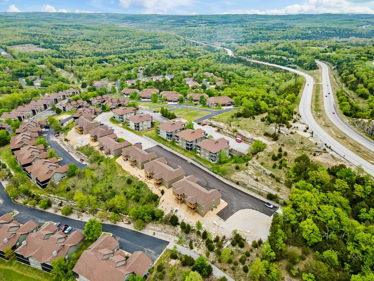 An aerial view of a quiet, green neighborhood layout surrounded by natural landscapes, roadways, and a nearby highway. Pathways and trails are visible, emphasizing community walkability and access to expansive outdoor exploration.