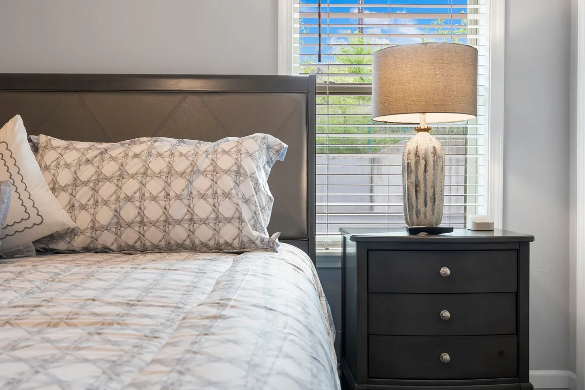 A serene interior bedroom scene featuring a bed with plush decorative pillows, a nightstand, and a softly lit table lamp. Natural light pours in, creating a tranquil atmosphere perfect for relaxation after a day on the greens.