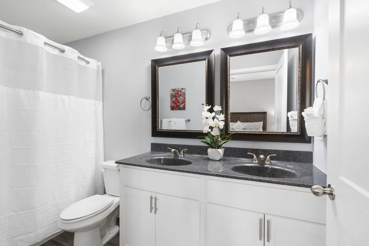 A bright, modern bathroom with a double sink vanity, large mirrors, and decorative flowers, creating a fresh and inviting space for morning routines or evening relaxation.