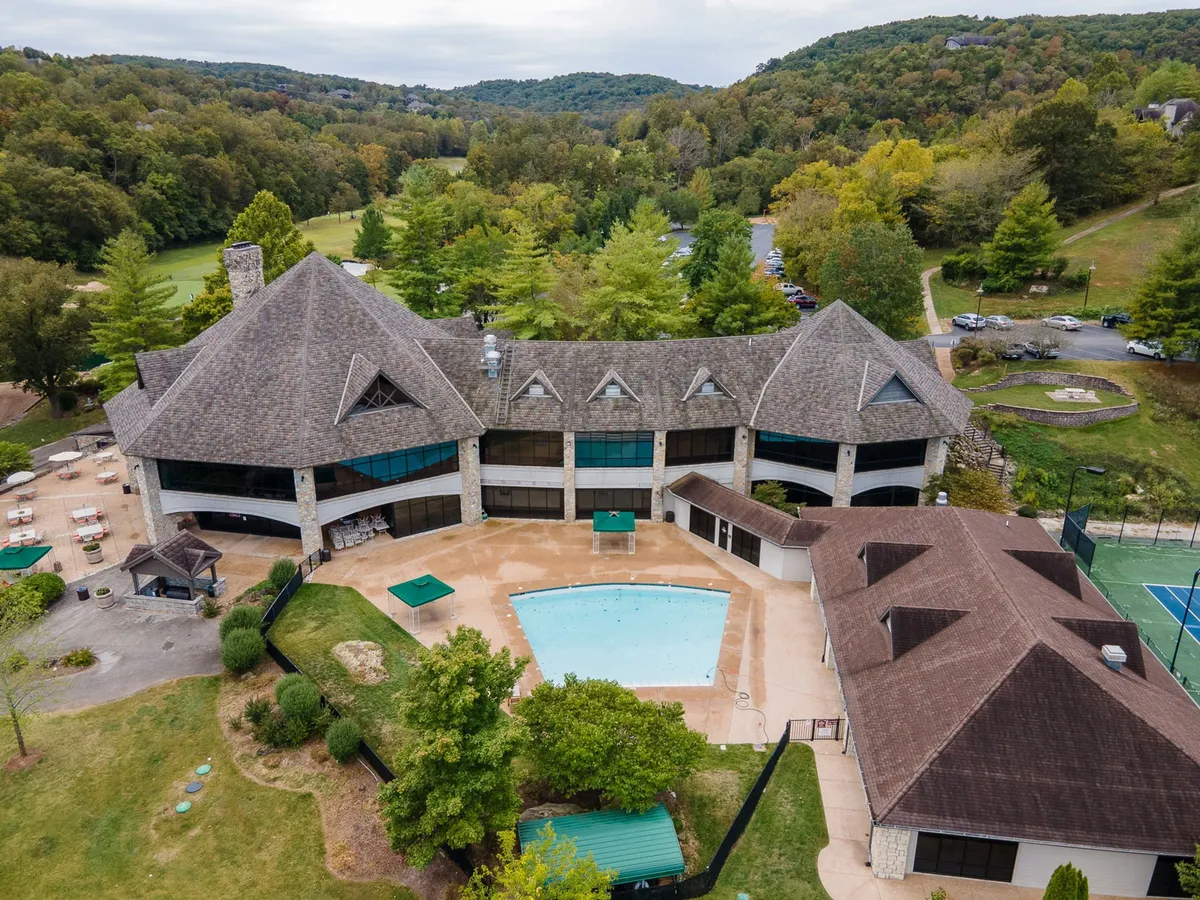 A bright outdoor swimming pool set amid landscaped gardens, with tennis courts and inviting architectural features in the background. The space looks lively yet relaxing, perfect for summertime fun.