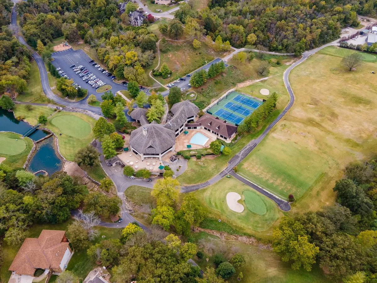 This vibrant exterior image captures the heart of StoneBridge Resort's amenities, including the golf course, swimming pool, tennis courts, clubhouse, and adjacent parking lot. The landscape is lush and inviting, showcasing spaces where guests can enjoy recreation and relaxation year-round.