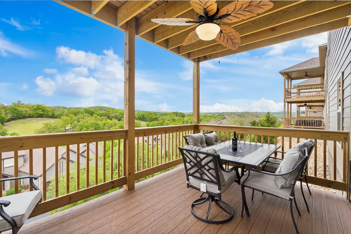 A spacious outdoor deck with a dining table, several comfortable chairs, and a ceiling fan overhead. The deck offers an inviting view of the surrounding hills and landscape, making it perfect for outdoor meals, socializing, and relaxation.