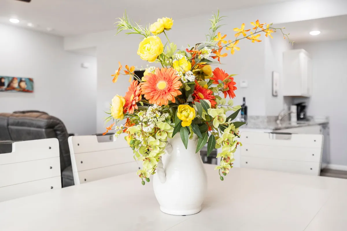 A cheerful dining area with a vase of flowers on the table, the kitchen visible in the background. The light and welcoming mood sets the scene for gatherings, meals, and everyday celebrations.