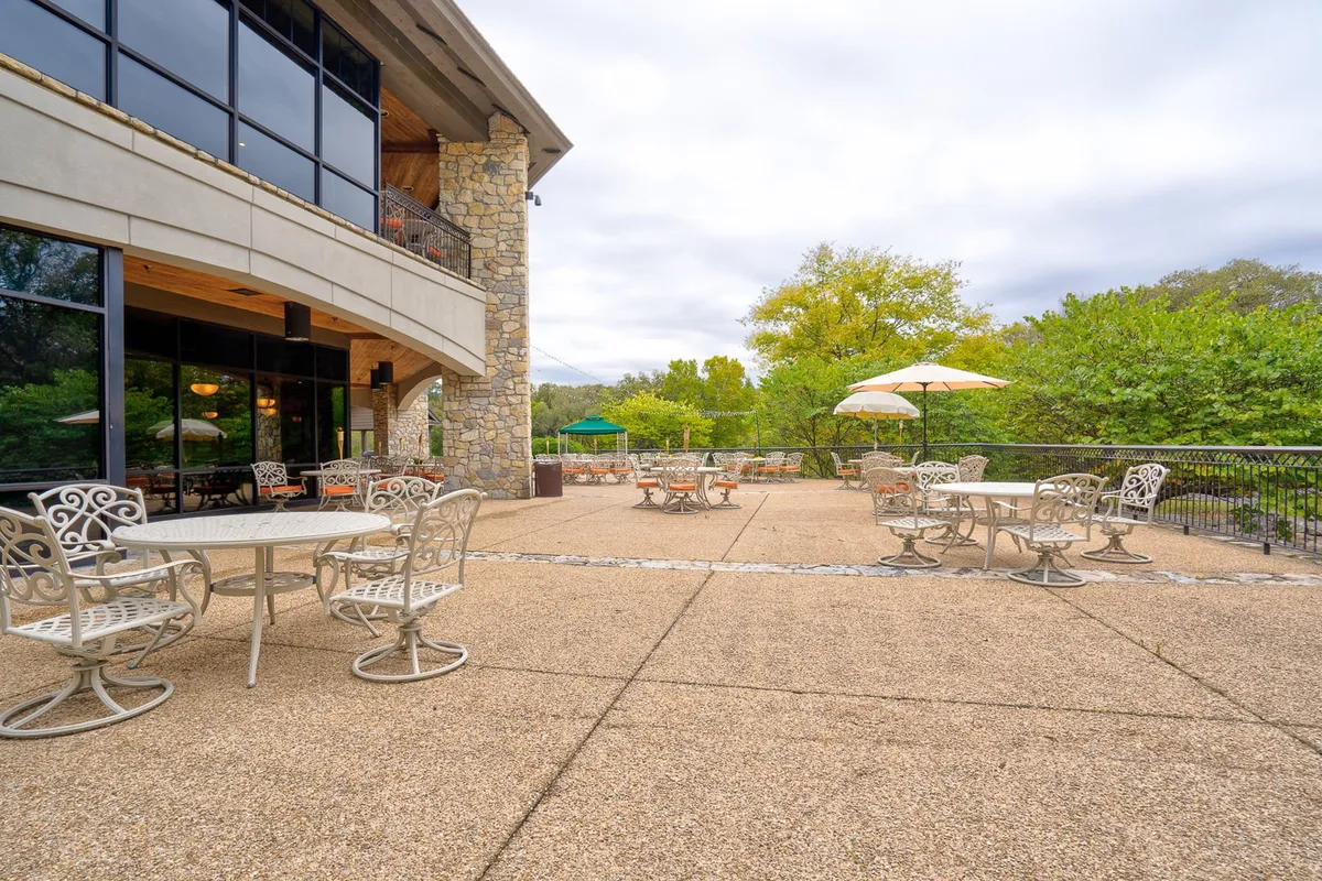 This exterior image features inviting outdoor seating areas with umbrellas, lush green trees, and the building facade in the background. The atmosphere is serene and welcoming, suggesting a perfect spot for dining al fresco or enjoying an evening drink under the stars.