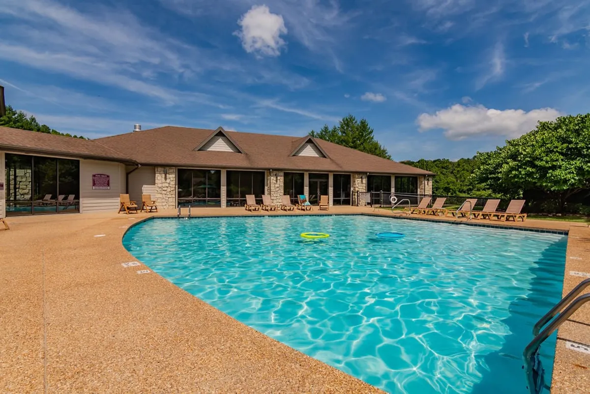 A sparkling outdoor swimming pool surrounded by lounge chairs and a building with expansive windows. The scene exudes a relaxed, vacation-like atmosphere ideal for sunbathing and socializing during the summer season.