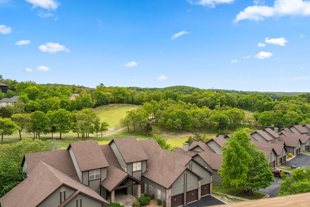 This image captures a panoramic view of the Ledgestone Golf Course with green lawns stretching out in front of a row of elegant townhouses. The scene conveys the proximity of the residences to the championship course, and the relaxed yet exclusive atmosphere is heightened by the soft light, likely during sunset or early morning.